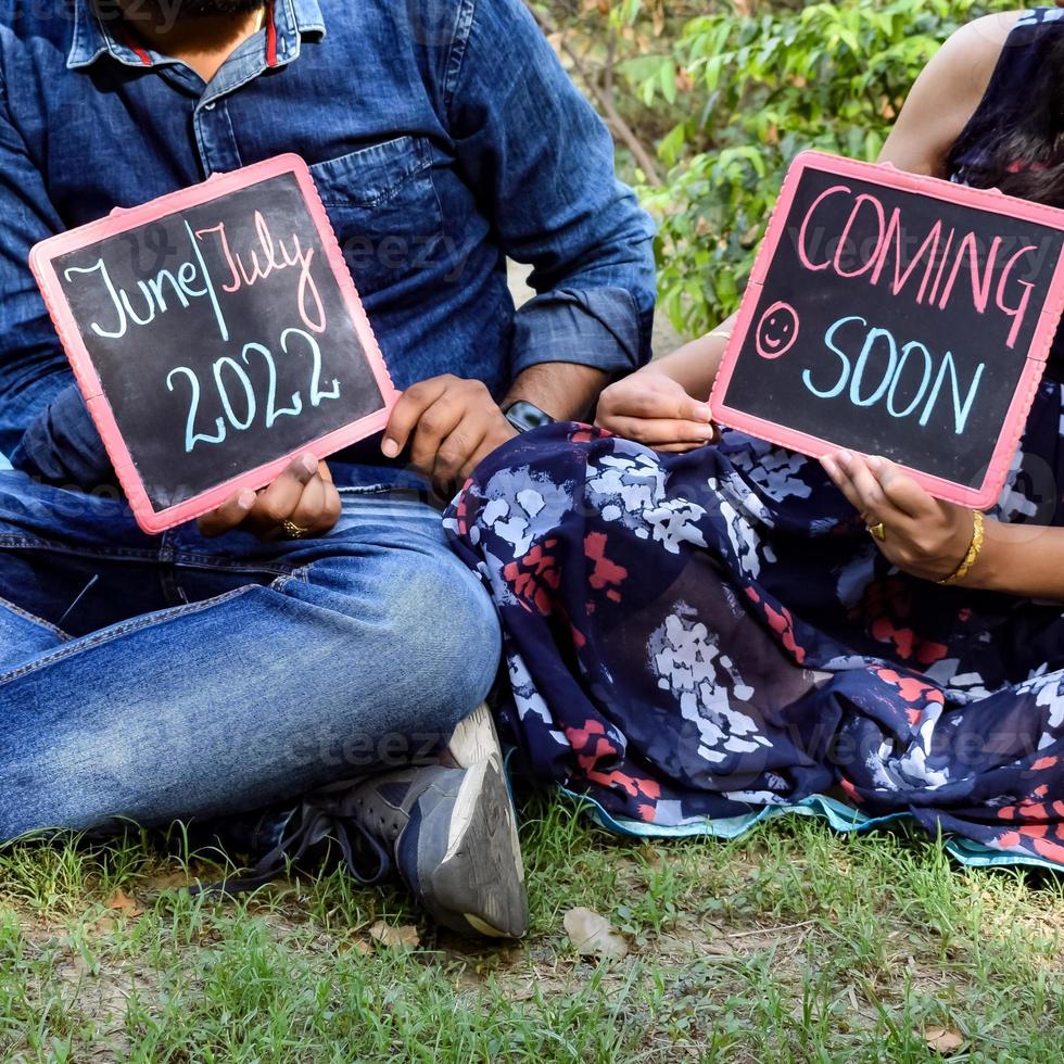 Indian couple posing for maternity baby shoot. The couple is posing in a lawn with green grass and the woman is falunting her baby bump in Lodhi Garden in New Delhi, India photo