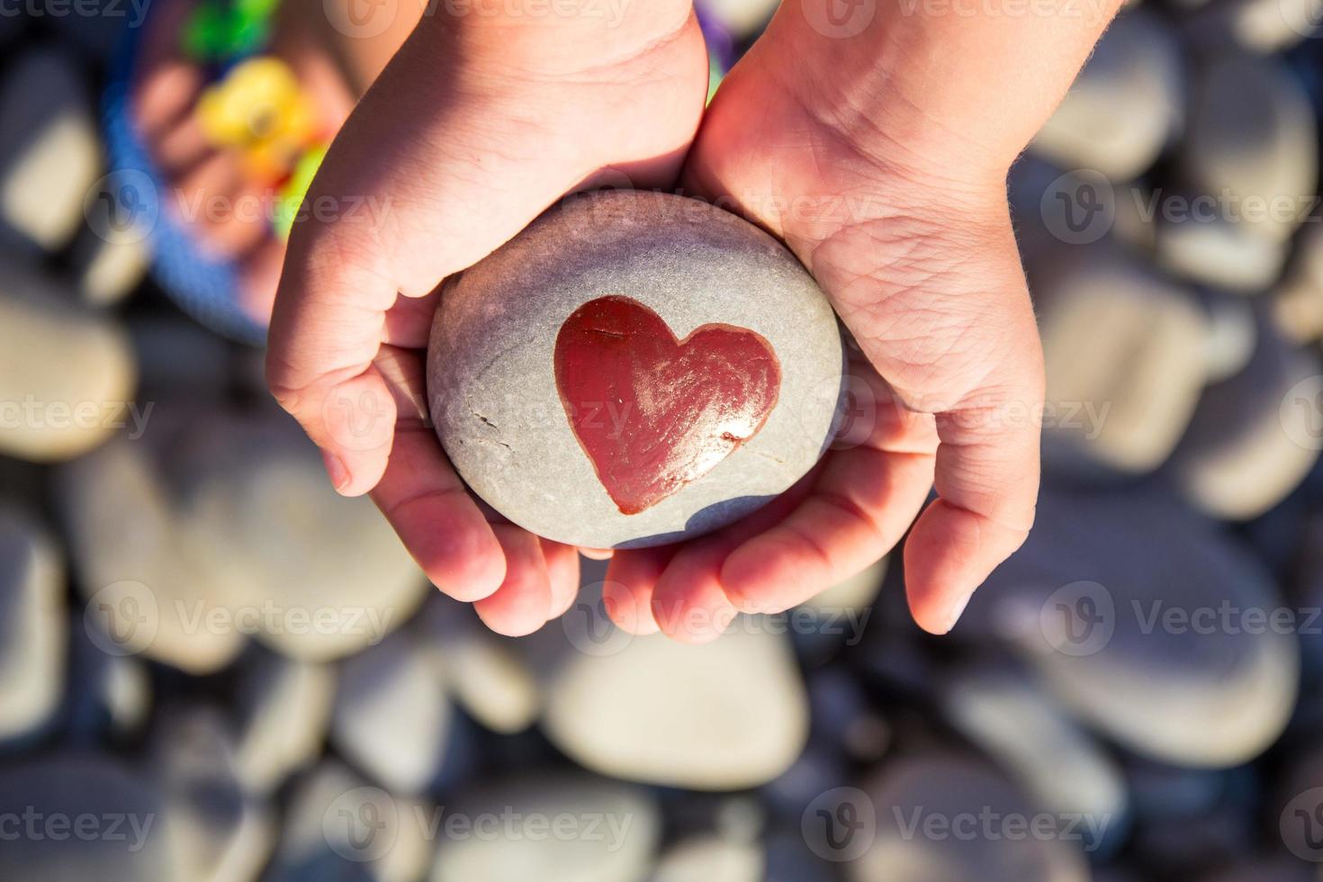 pebbles with a painted heart in the hands of a child on the background of a pebble beach photo