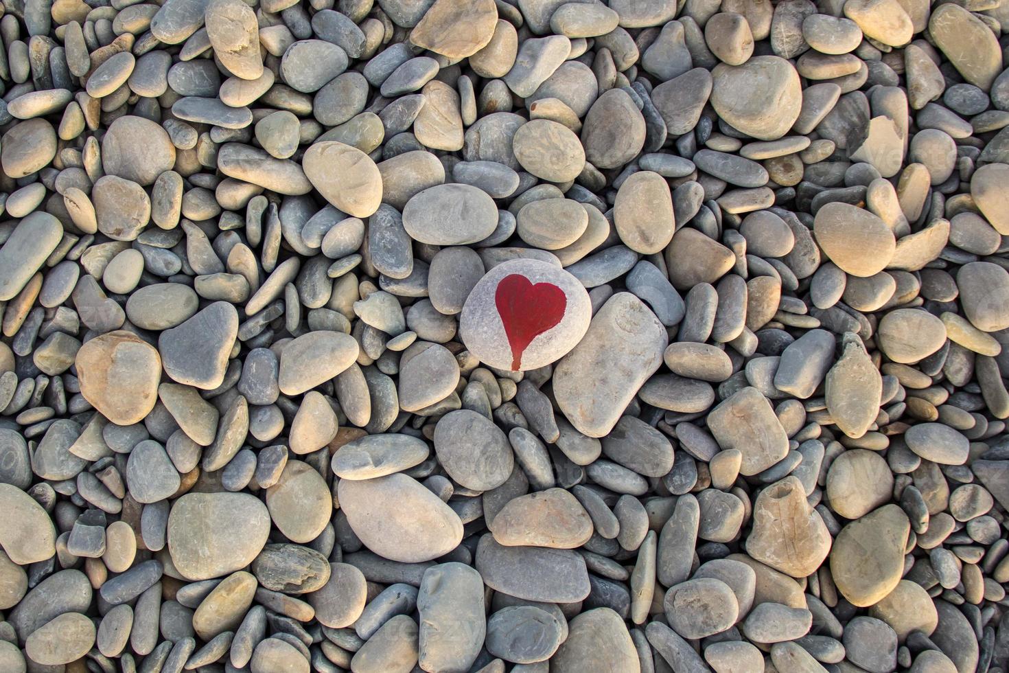 stone heart painted with a red paint marker on the pebble as a gift for Saint Valentine day on the pebble background. photo