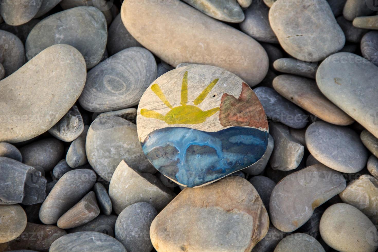 Bright sun painted on pebble. Pebbles and sea background. photo