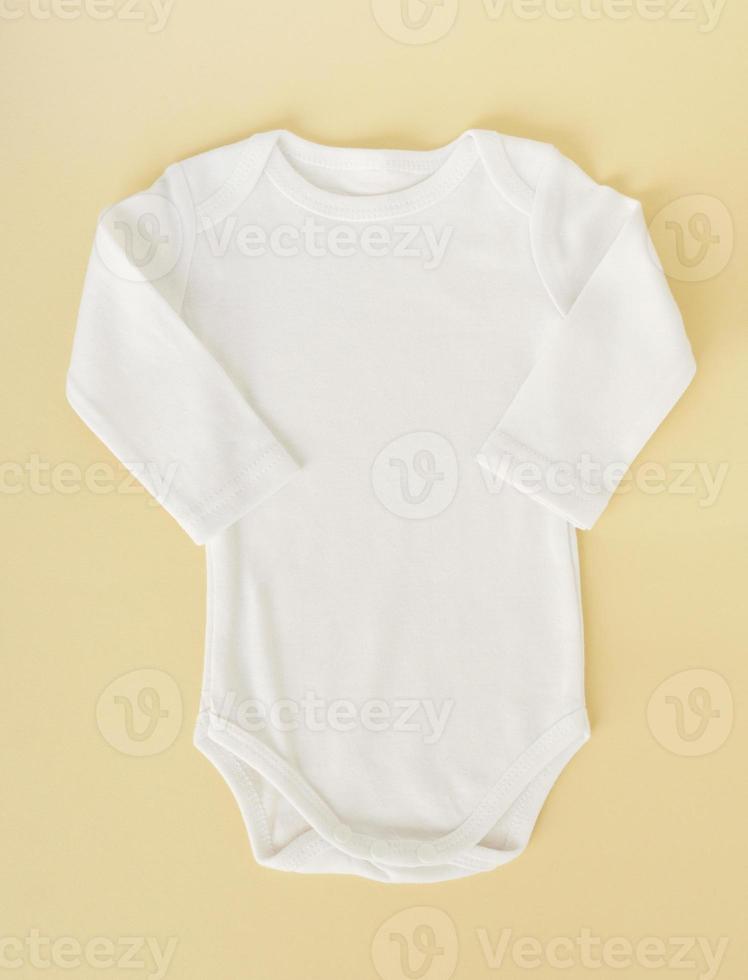 ropa de bebé blanca sobre un fondo amarillo, puesta plana. maqueta para diseño foto