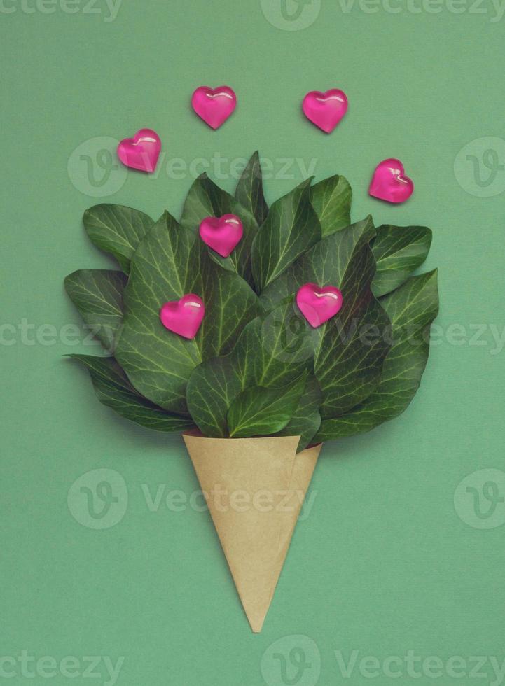 An unusual bouquet with hearts and green leaves in a paper wrapper. Creative Valentines Day greeting card. photo