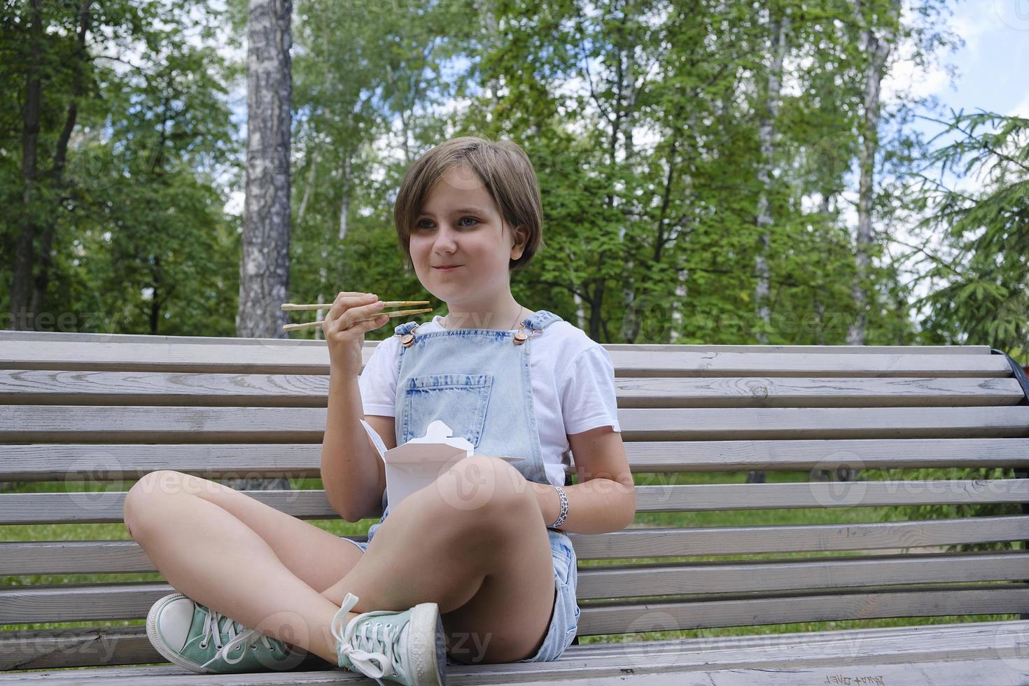 a teenage girl on a walk on a summer day in the park has lunch with noodles wok photo