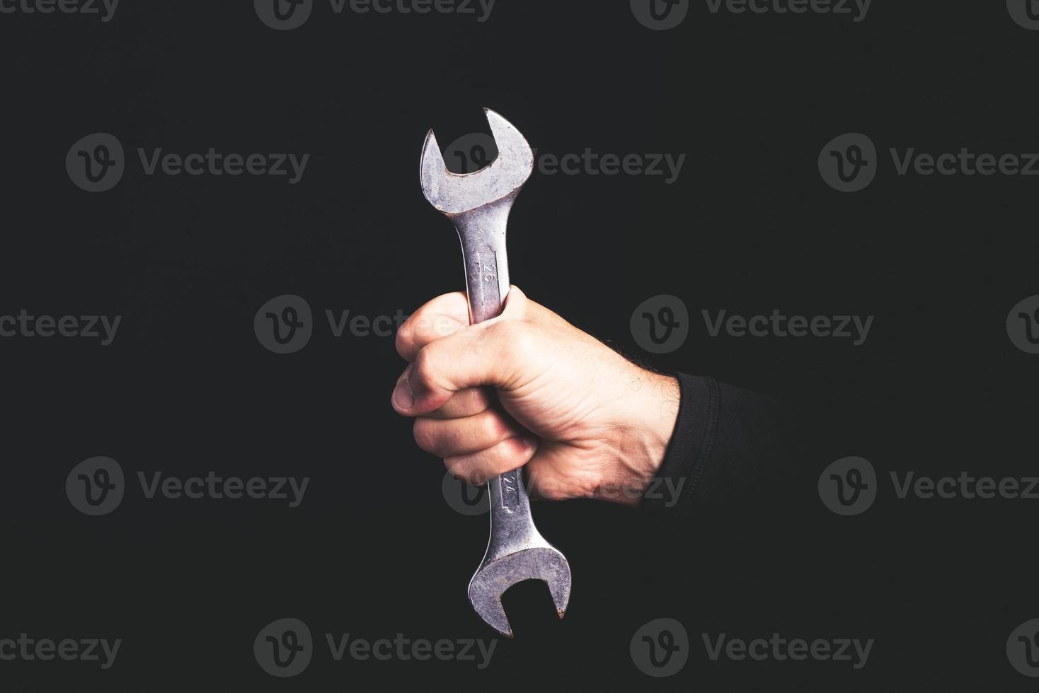 spanner tool in a man hand on black background - maintenance sercice concept photo