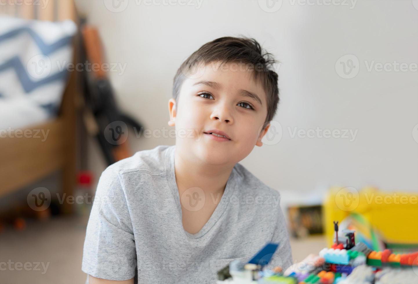 Portrait kid playing plastic blocks, Happy Child relaxing sitting on carpet building his colourful blocks toys in bedroom, Young boy with smiling face looking at camera while holding toy. photo