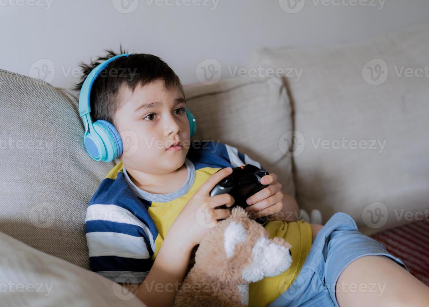 niño de vista lateral de retrato usando auriculares y jugando videojuegos.  niño sosteniendo un juego de consola en línea en casa, un niño sentado en  un sofá divirtiéndose y relajándose solo el