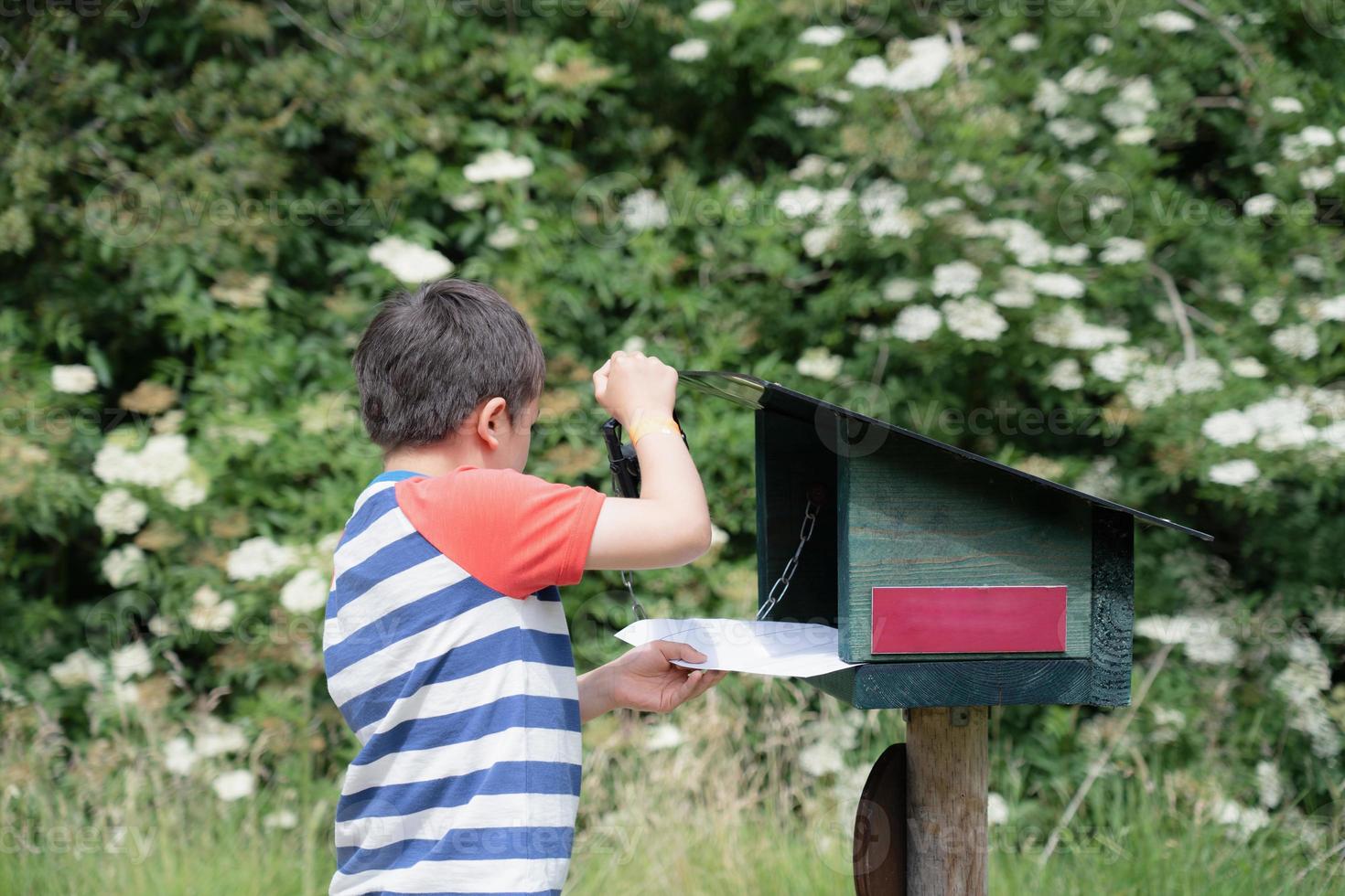 Kid using ink stamp on white paper,Boy standing at ink stamp trail station,Child explorer and learning about wild nature,Kid having fun with outdoors activity or adventure in forest with school trip photo