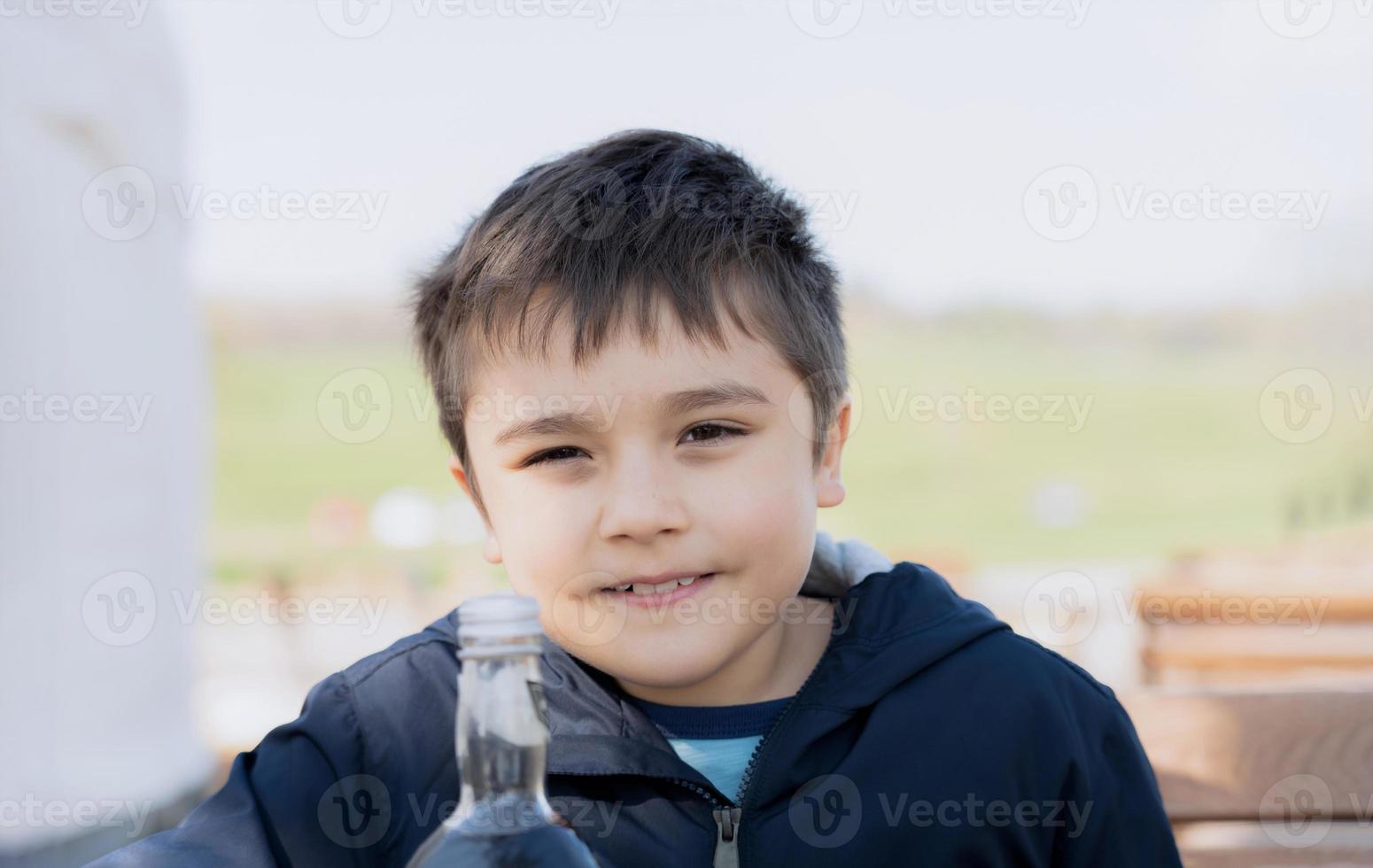 High key portrait Kid looking at camera with smiling face, Happy young boy sitting outdoor cafe witing for food, Positive Child relaxing outdoor in Sunny day Spring or Summer photo