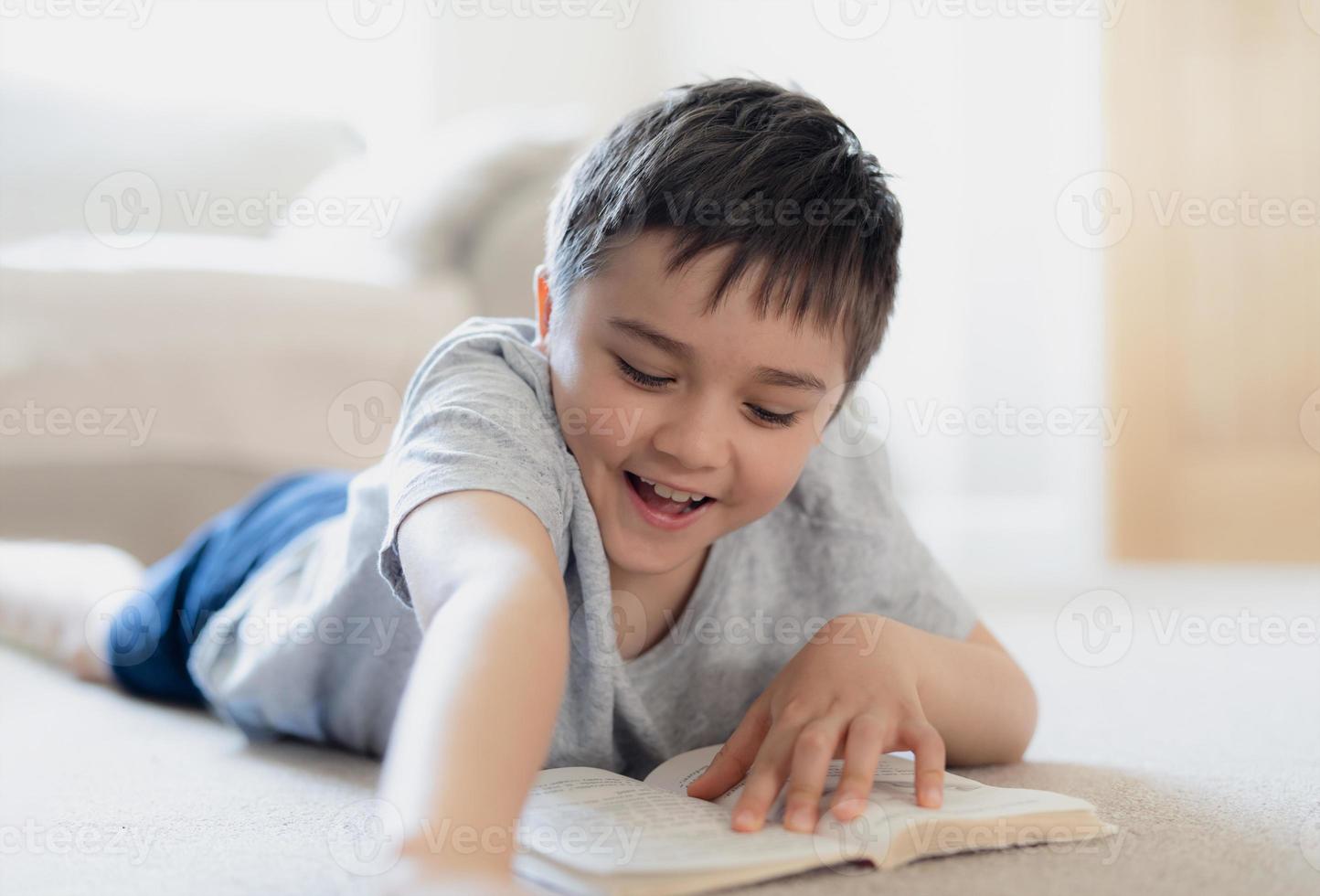 Portrait School kid reading a book for homework, Young boy lying on carpet enjoy reading the story in living room, Child relaxing at home on weekend. Home Schooling or Education concept photo
