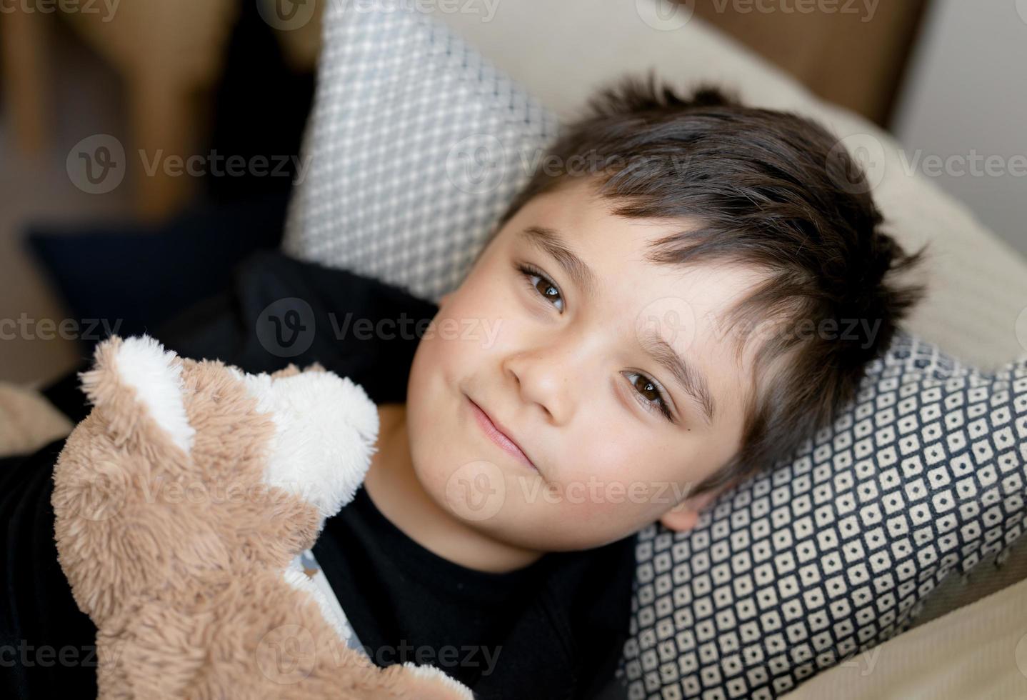 Happy boy lying on sofa looking up at camera with smiling face,Positive Child resting in living room with bright light shining from window on sunny day spring or summer.Kid relaxing at home on weekend photo