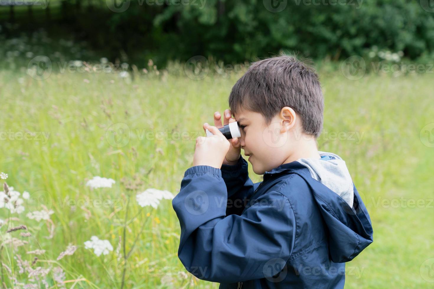 Kid looking through mini microscope with wondering face, Excited Child on a camping school trip in green forest, Kid explorer with wildlife nature in summer camp, Travel and Education concept photo