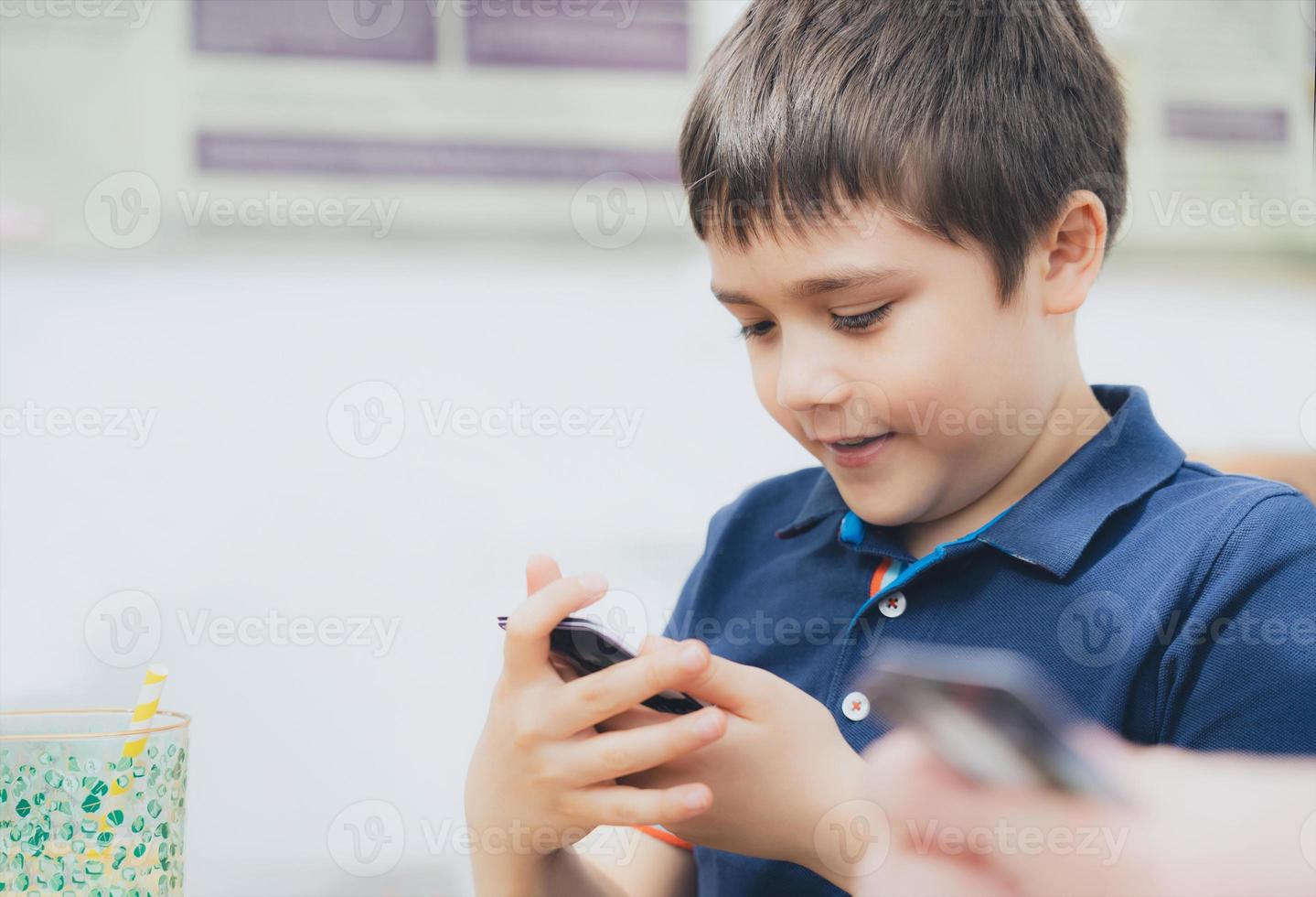 Young boy playing card game in the cafe while waiting for food, Kid with curious face looking at paper card on his hands,  Family playing board game indoor on sunny day spring or Summer. photo