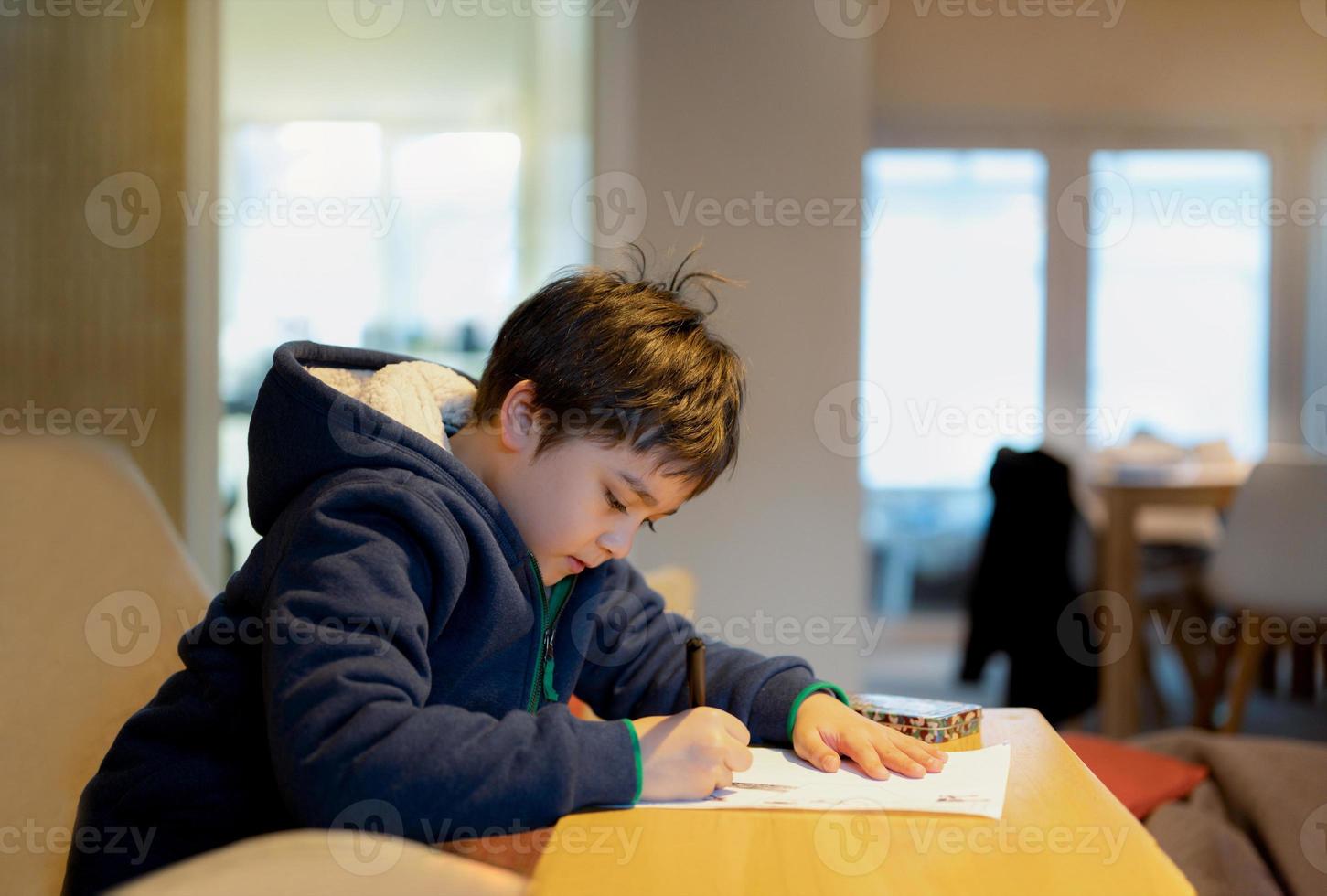 niño de la escuela usando un bolígrafo negro dibujando o escribiendo la carta en papel, un niño haciendo la tarea, un niño con un bolígrafo escribiendo notas en una hoja de papel durante la lección. alumno lindo haciendo la prueba, concepto de educación en el hogar foto