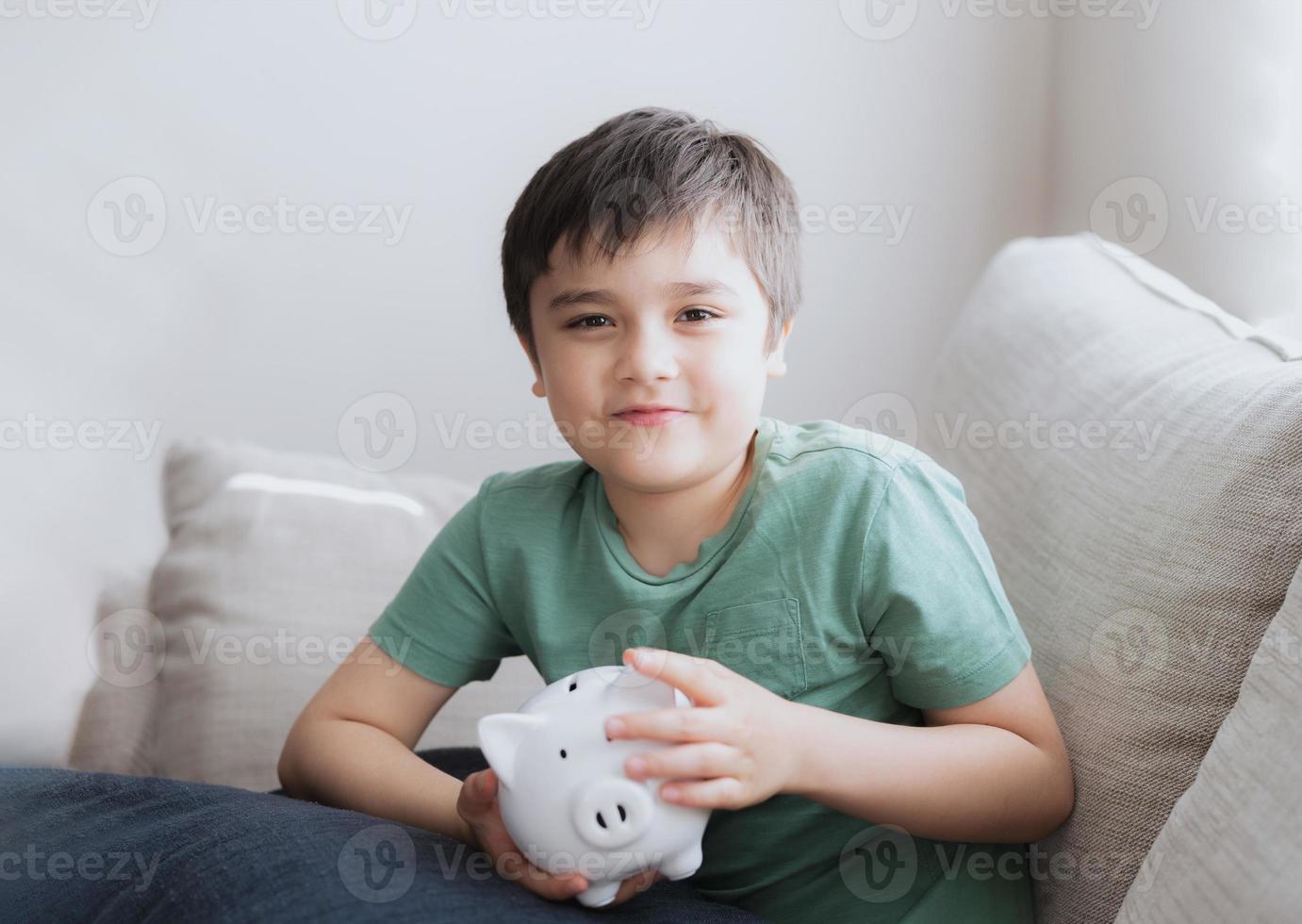 Happy boy holding piggy bank with smiling face. Indoor portrait of a cheerful child showing money saving box.School kid Learning financial responsibility and planning about saving for future concept photo