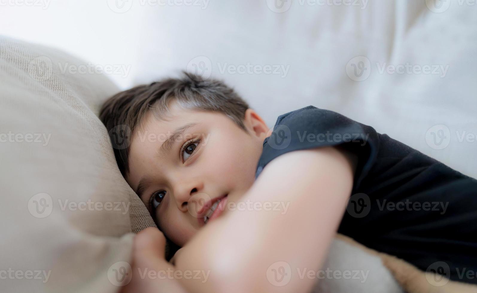 retrato cinematográfico niño feliz acostado en el sofá mirando con cara sonriente, niño positivo descansando en la sala de estar con luz brillante que brilla en primavera o verano. niño relajándose viendo la televisión el fin de semana foto