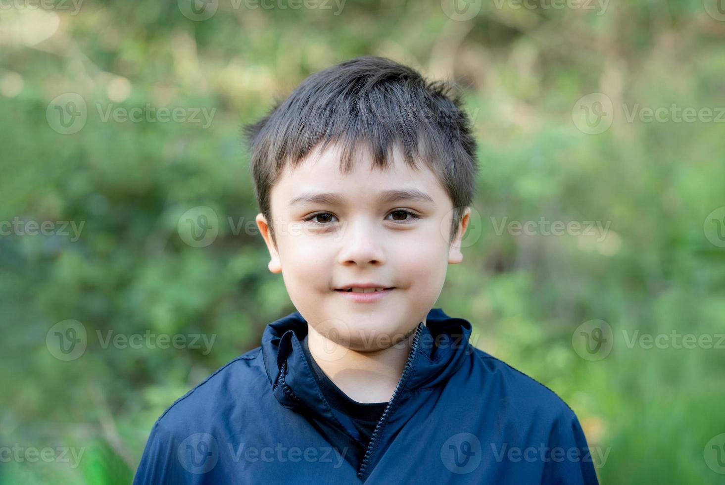 Outdoor portrait handsome young boy looking at camera with smiling face, Healthy kid with a happy face standing alone in the park, Positive child playing outside in Spring or Summer Holiday photo
