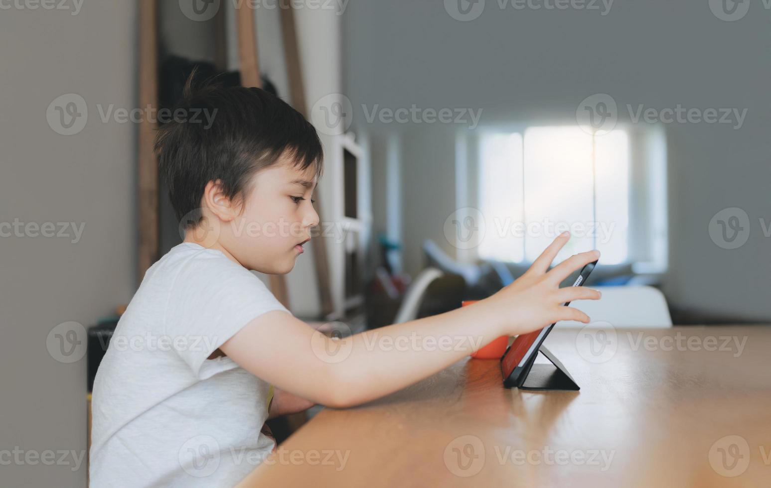 Kid playing game online with friends on tablet, Cinematic portrait young boy video call with friends while having breakfast,Child watching cartoon on internet, School kid doing homework on digital pad photo