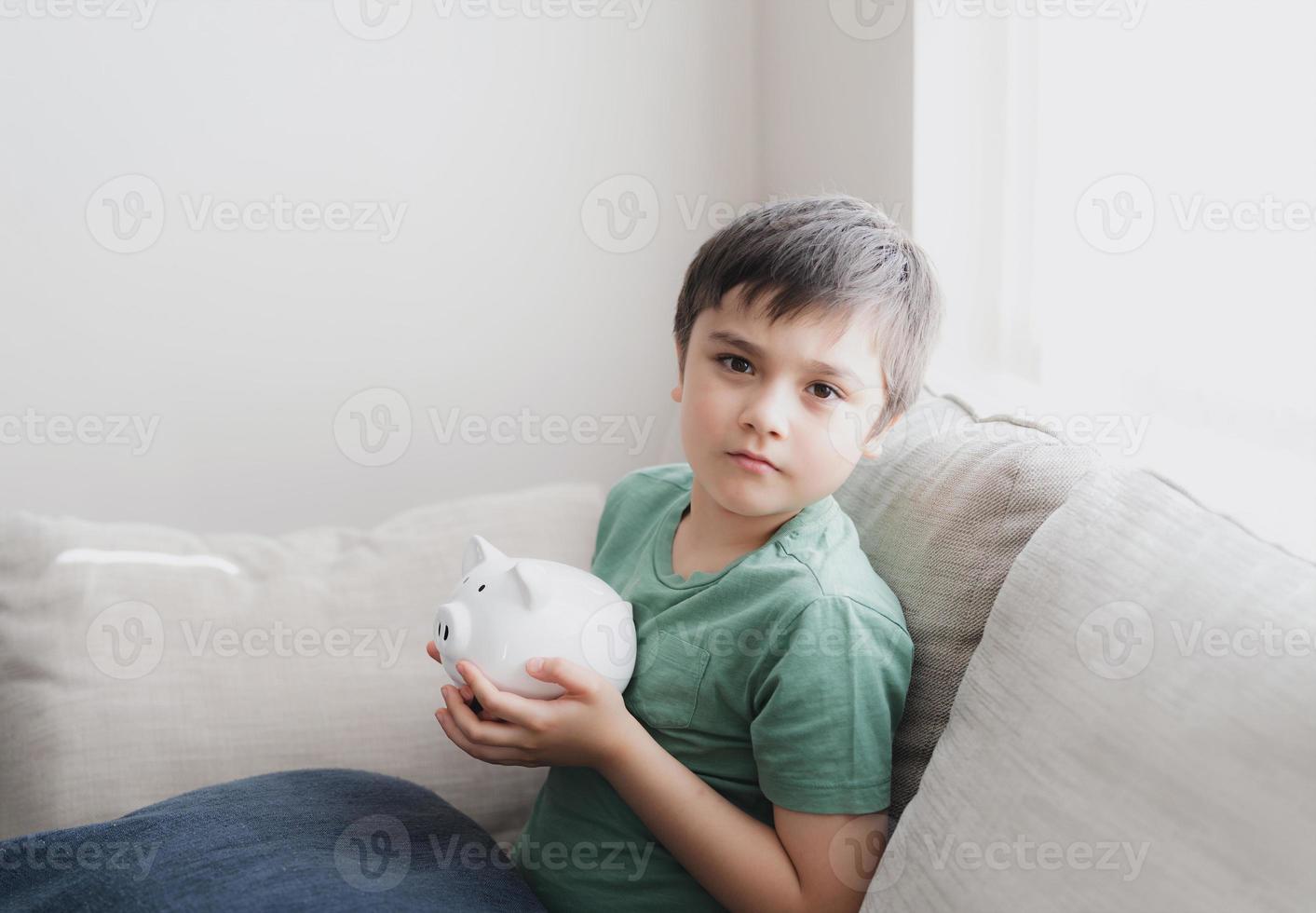 niño feliz sosteniendo alcancía con cara sonriente. retrato interior de un niño alegre que muestra una caja de ahorro de dinero. niño de la escuela aprendiendo responsabilidad financiera y planificando el ahorro para el concepto futuro foto