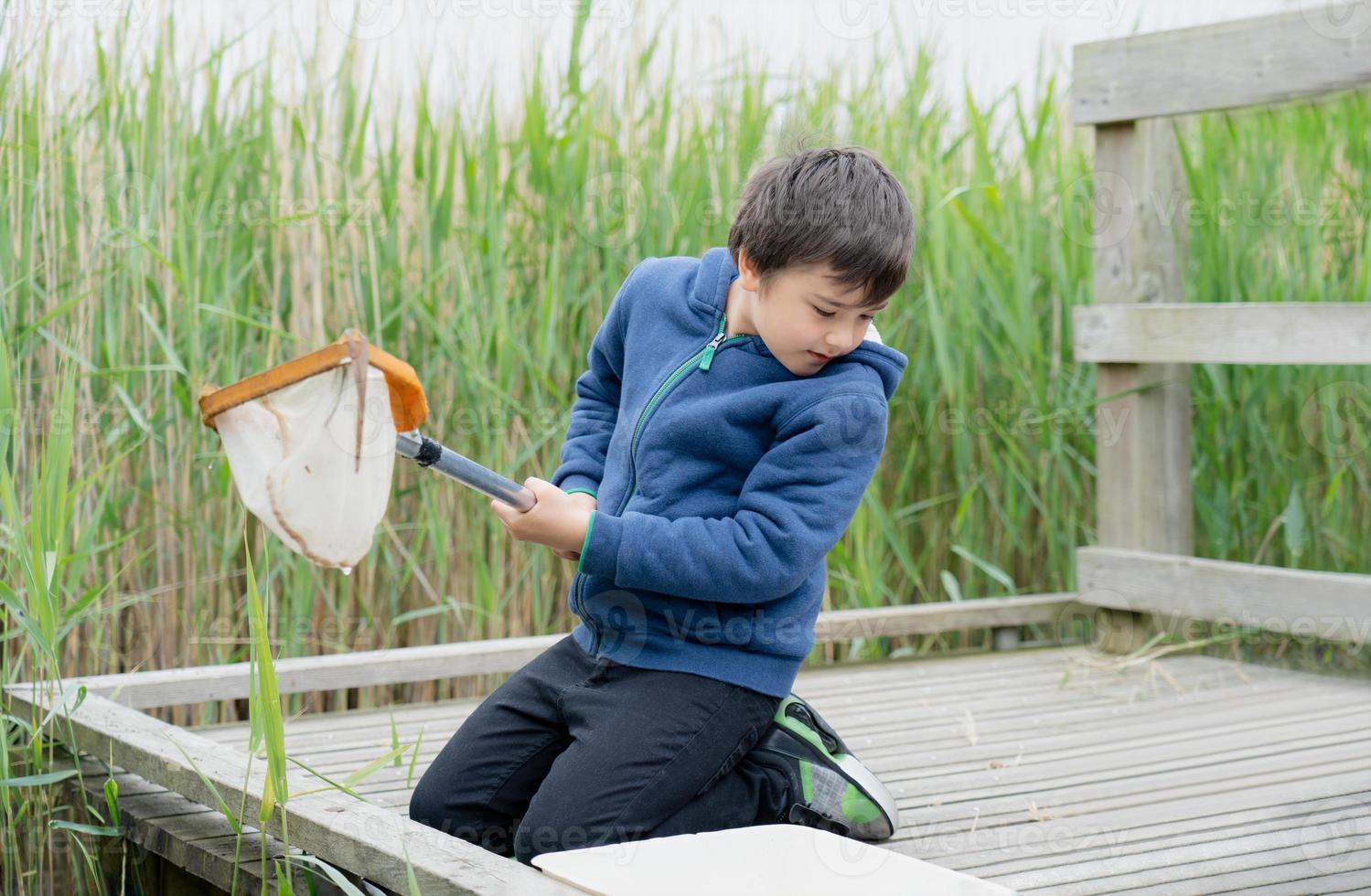 Portrait Kid boy using fishing landing net catching creatures in pond with net in Spring time,  Child explorer and learning about wild nature in countryside, Summer camp outdoors activity for children photo