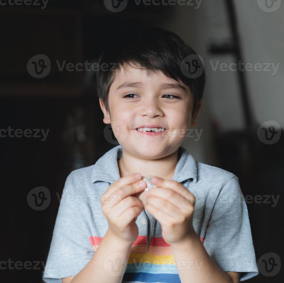 Happy kid looking out with smiling face, Child playing alone  in living room, Selective focus Child boy holding one pound coin looking out ,  Children learning to save money for studying or future photo