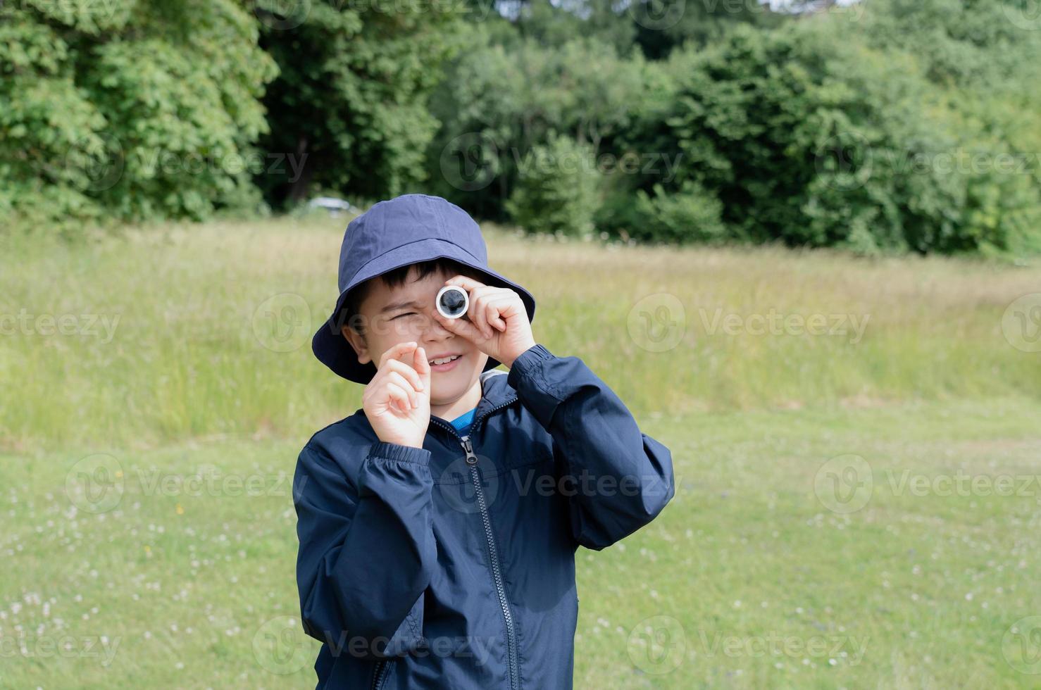 niño mirando a través de un mini microscopio con cara de asombro, niño emocionado en un viaje escolar de campamento en un bosque verde, niño explorador con la naturaleza de la vida silvestre en el campamento de verano, concepto de viaje y educación foto