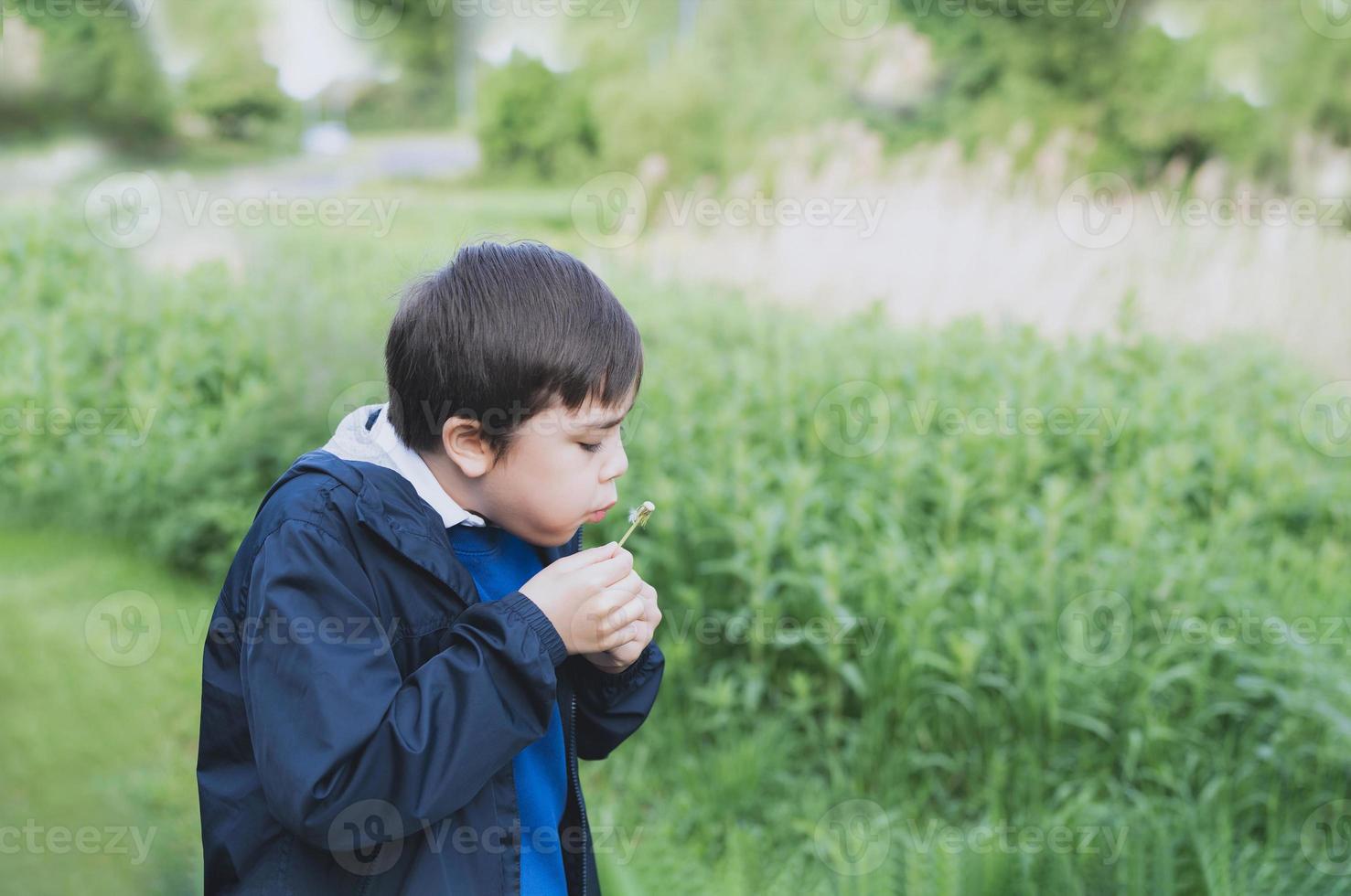 un lindo niño de la escuela que sopla una flor de diente de león en el parque de primavera mientras camina a la escuela por la mañana. niño feliz niño divirtiéndose al aire libre. foto