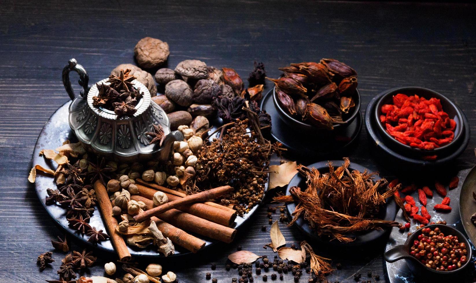 foto de vista superior Se colocaron montones de ajo, cebollas, pimientos, chile y hierbas secas en platos y tazas sobre un fondo de madera negra. se dividió para preparar para cocinar comida india comida saludable