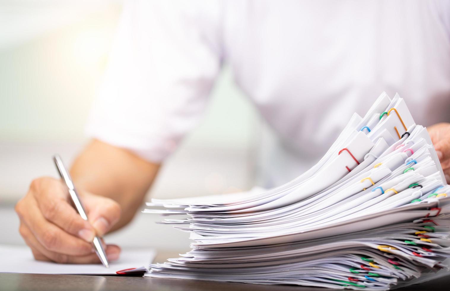 Man in a white shirt sign contract agreement documents in Stack of Group report papers clipped in color clips in fair light, business, legal law and education concept photo