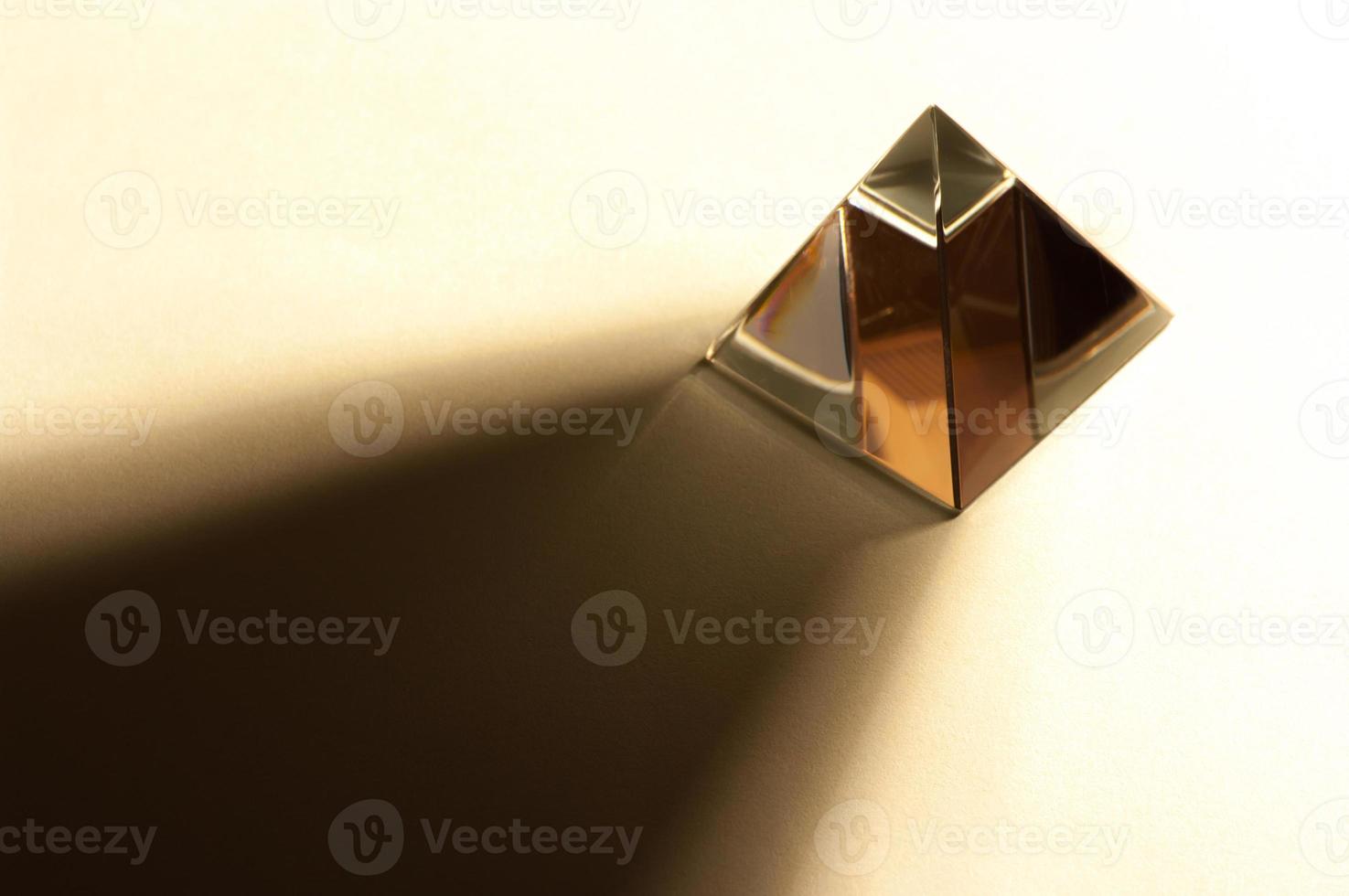Minimalist still life image of a shiny pyramid in warm color tone. Pyramid throwing hard shadow. photo
