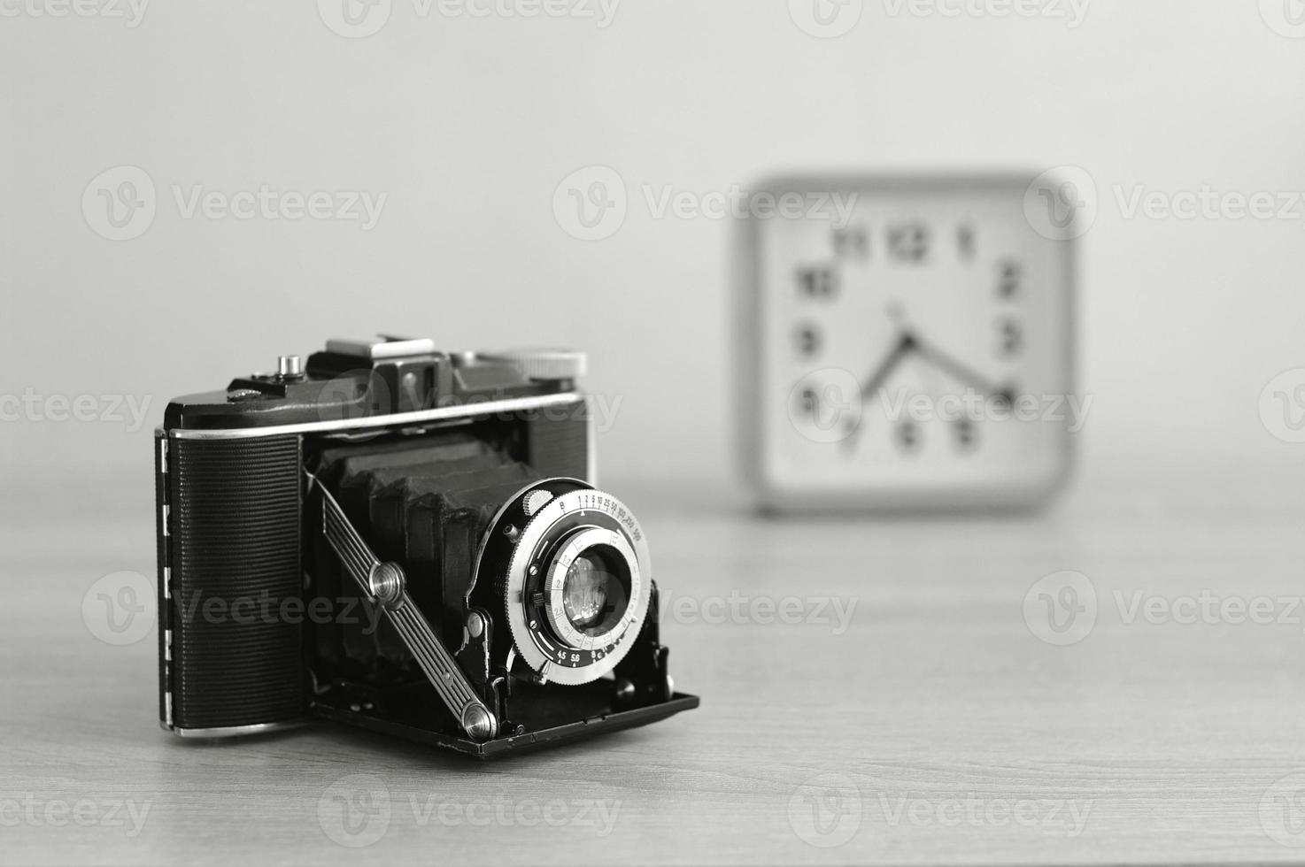 Vintage analog medium format film camera and a clock in black and white. Old film camera with bellows. photo