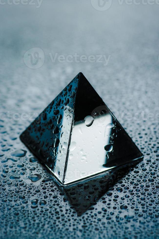 Shiny geometric object with drops of water. Wet trasparent pyramid close up view. photo