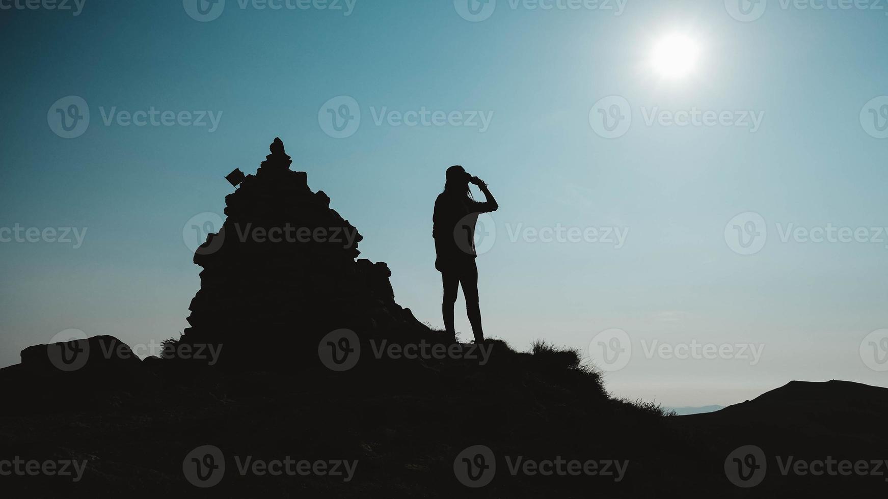 Silhouette of woman standing on rock near the edge of mountain on background of sky photo