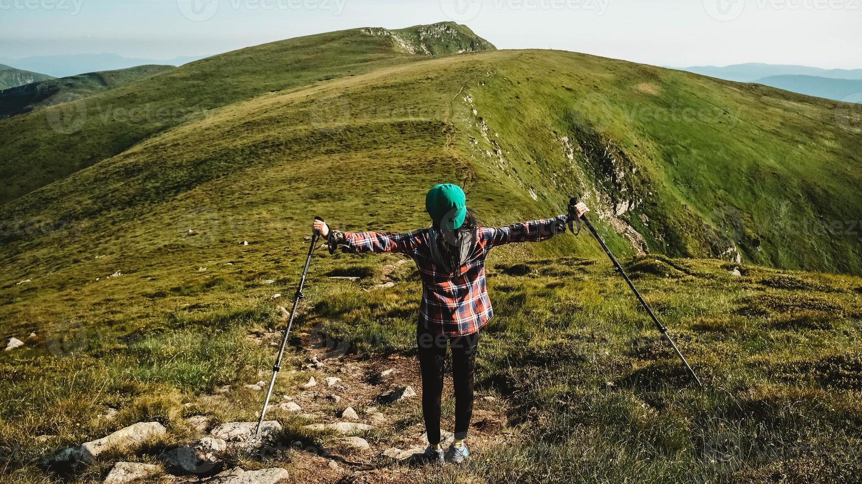 Woman tourist is walking on a hiking trail against background of green mountains photo