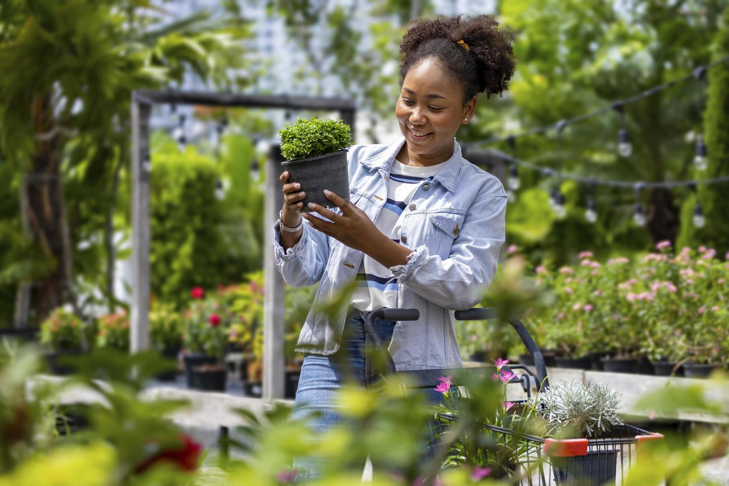 un joven cliente africano está eligiendo una planta exótica del vivero del centro de jardinería local con un carrito de compras lleno de plantas de verano para la jardinería de fin de semana y actividades al aire libre foto