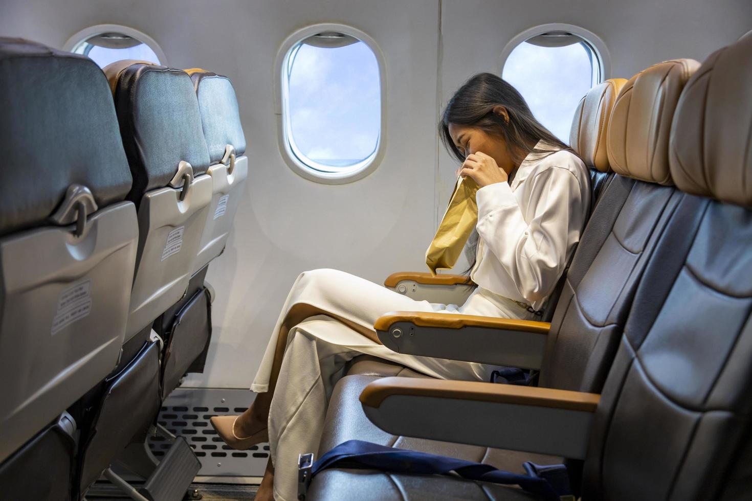 mujer asiática está vomitando en el avión durante el vuelo usando una bolsa de vómito debido al movimiento y la enfermedad del viaje que causan mareos por concepto de aerofobia y transporte foto