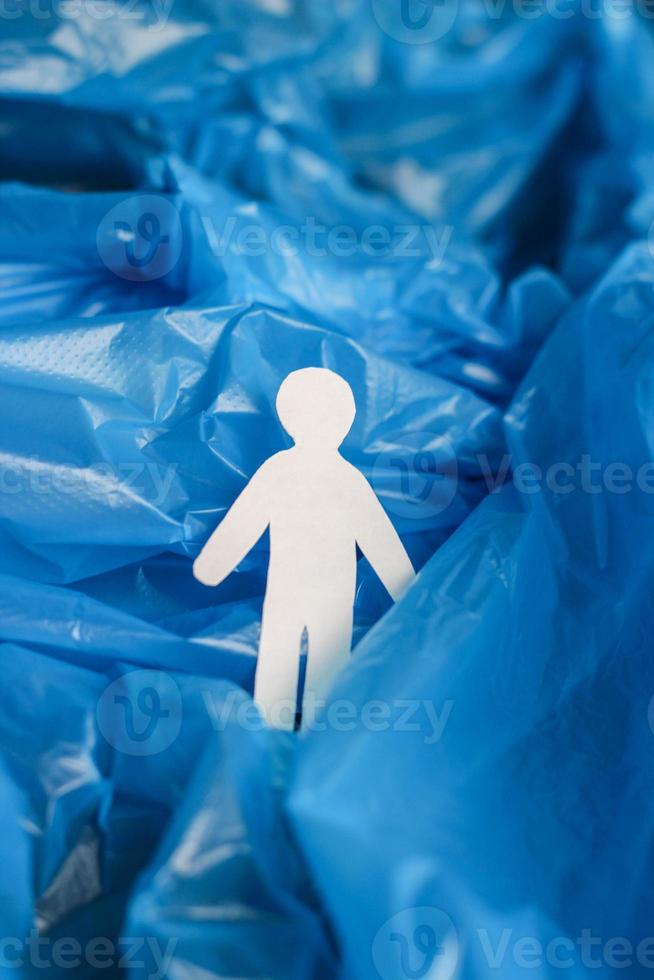 The silhouette of a man carved from white paper is immersed in a blue plastic bag as if in waves of water, ocean, sea. photo