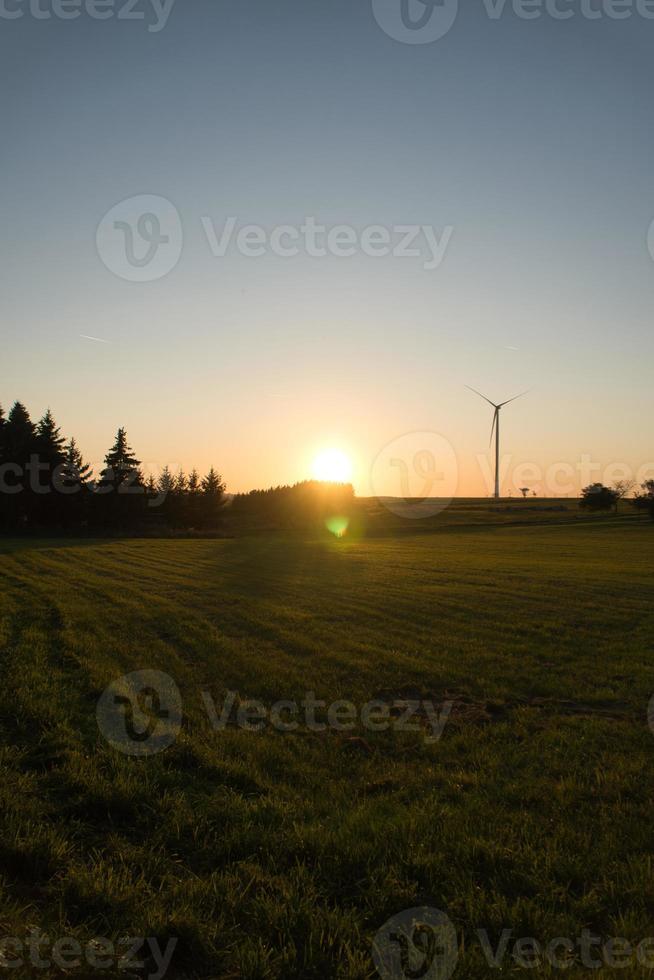 Wind turbine on a hill in front of a field and at the edge of the forest at sunset photo