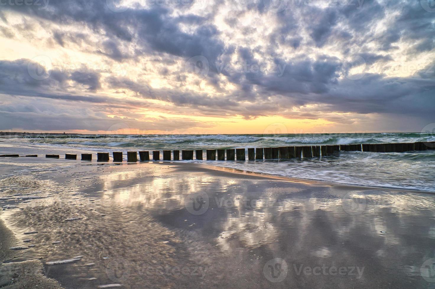 puesta de sol en la playa del mar báltico. reflejo en la playa. los espigones llegan al mar. foto