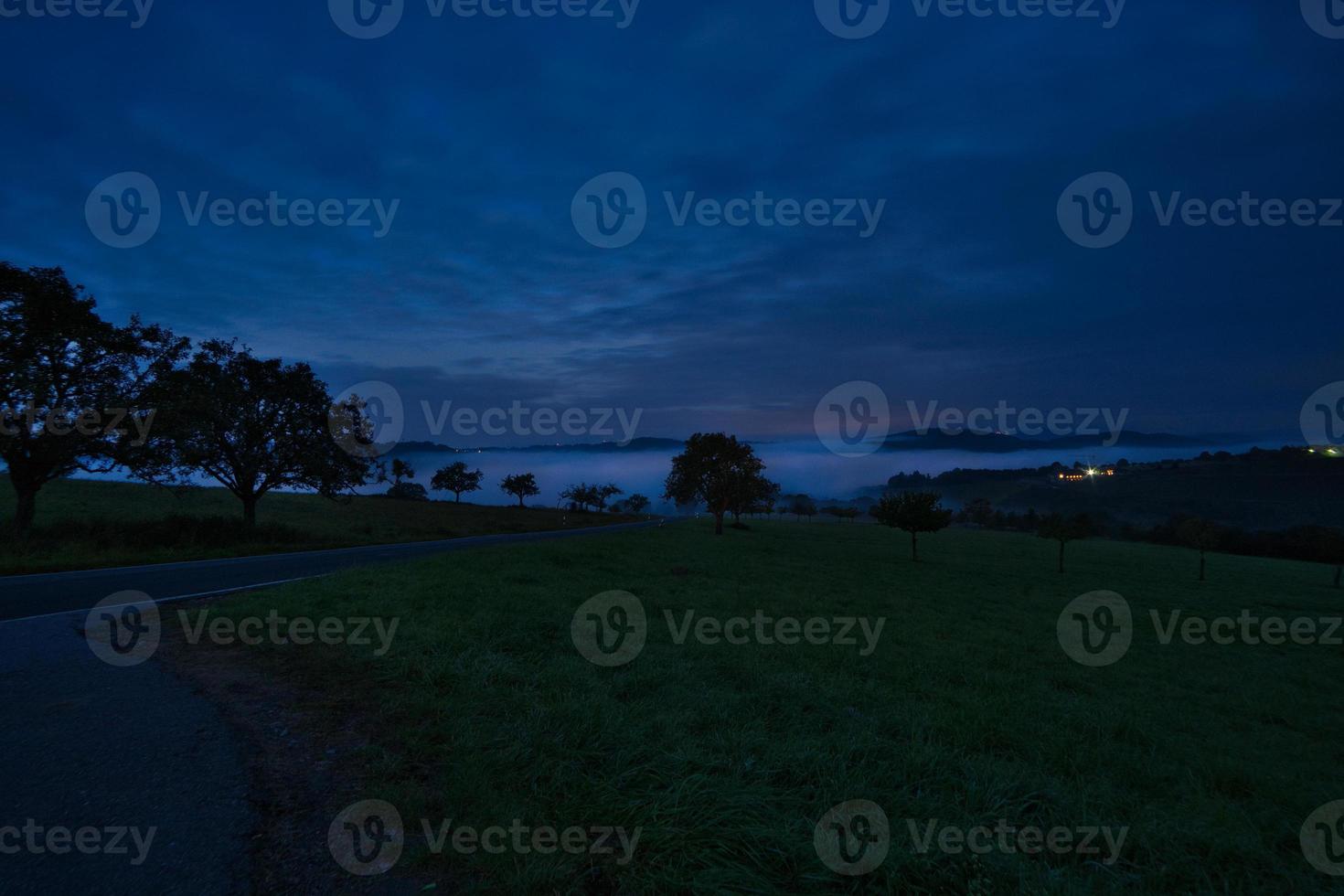 road with trees and meadows at blue hour in the evening. photo