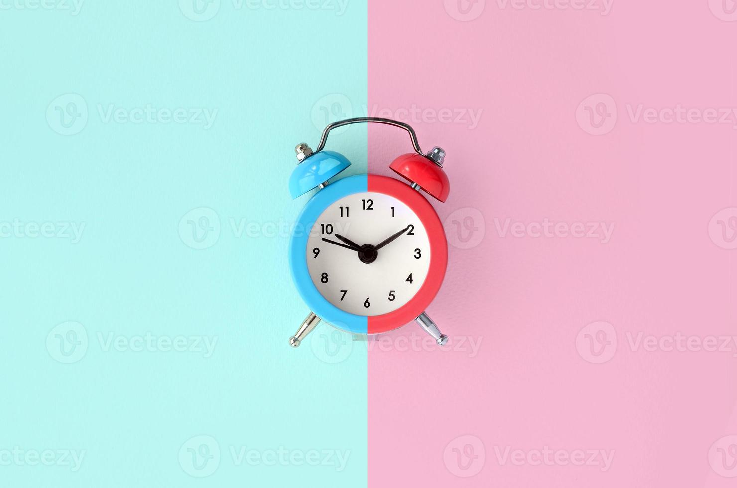 A small alarm clock is located between the blue and red background areas photo