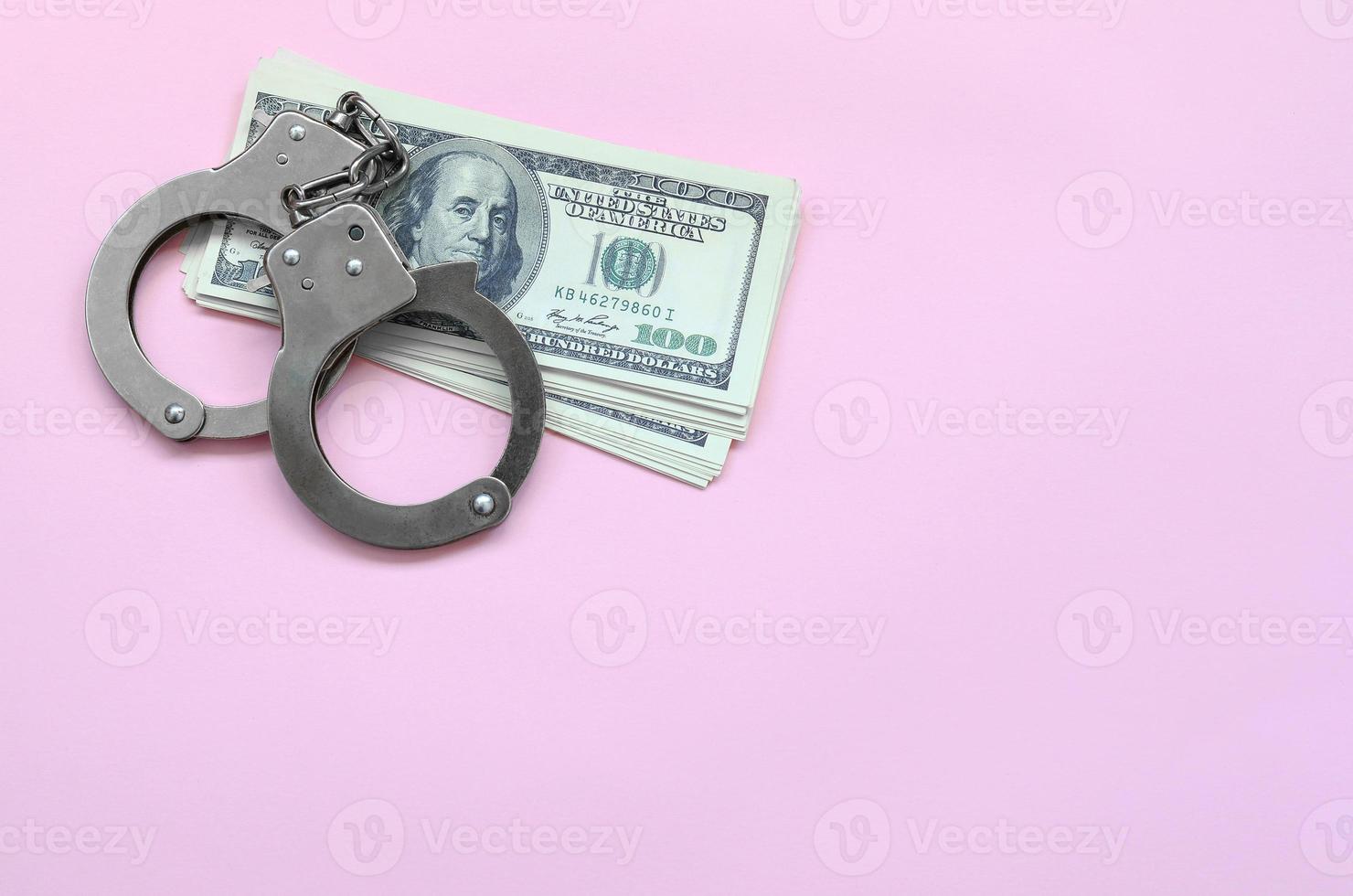 Police handcuffs and hundreds of us dollars lie on a pink background photo