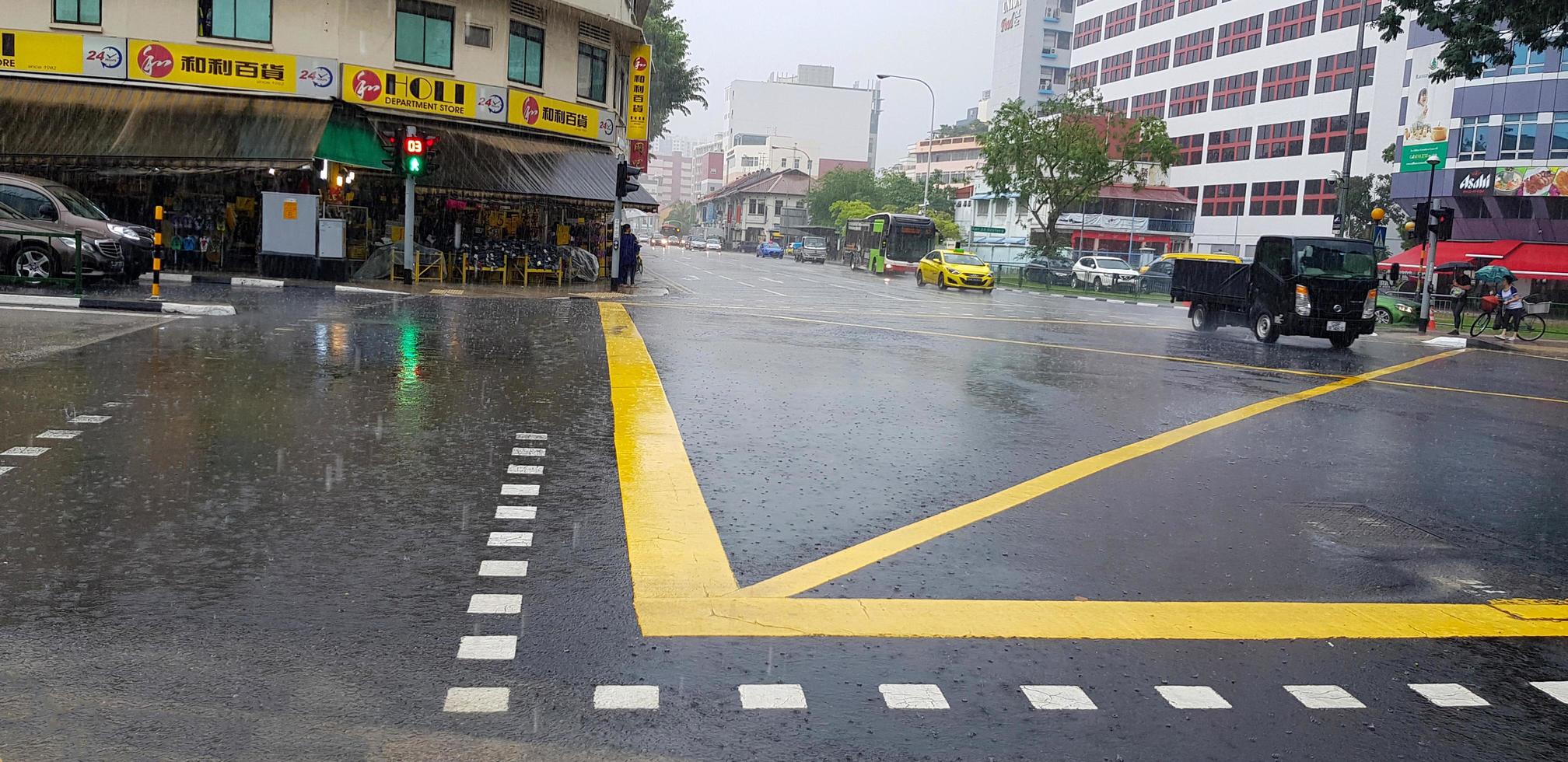 Singapore - June 28, 2021 Road crossing with heavy rain and yellow line on street with building and car background. Traffic on raining day and weather concept. photo