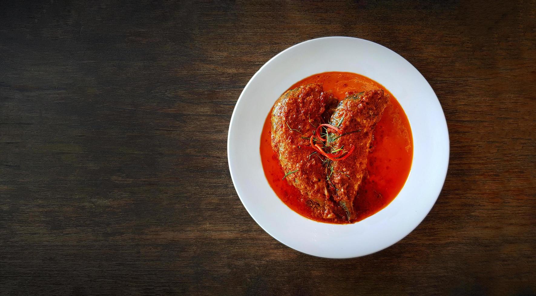 vista superior de la caballa fresca en salsa de curry rojo seco sobre un plato blanco o sobre una mesa de madera con espacio para copiar en el restaurante tailandés. Los tailandeses también llaman choo chee pla. endecha plana de comida famosa en tailandia. foto