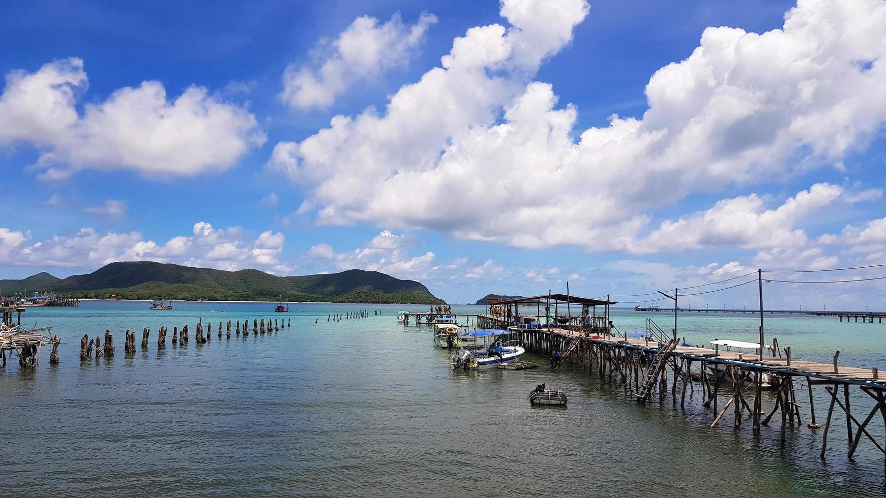 Wooden bridge pathway for group of people, tour, tourist walk to get in speedboat and longtail boat to take trip on sea go to island and fishing fish and squid with white clouds, blue sky background. photo