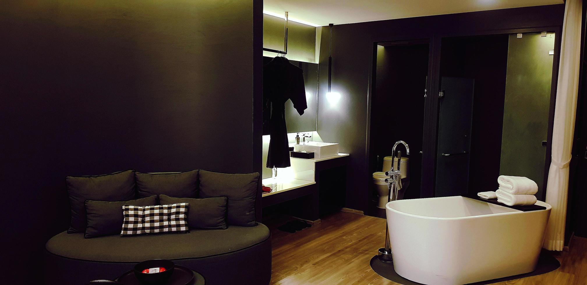 Modern room with white bathtub, dark gray or grey sofa, plaid pillow, basin and black bathrobe. Inside decorated in black tone style and wooden floor. Beautiful interior and furniture design. photo