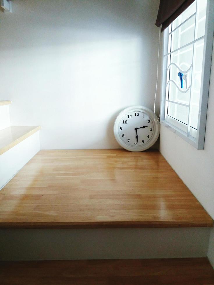 White vintage clock put on wooden step, stair or stairway with light  form window. photo