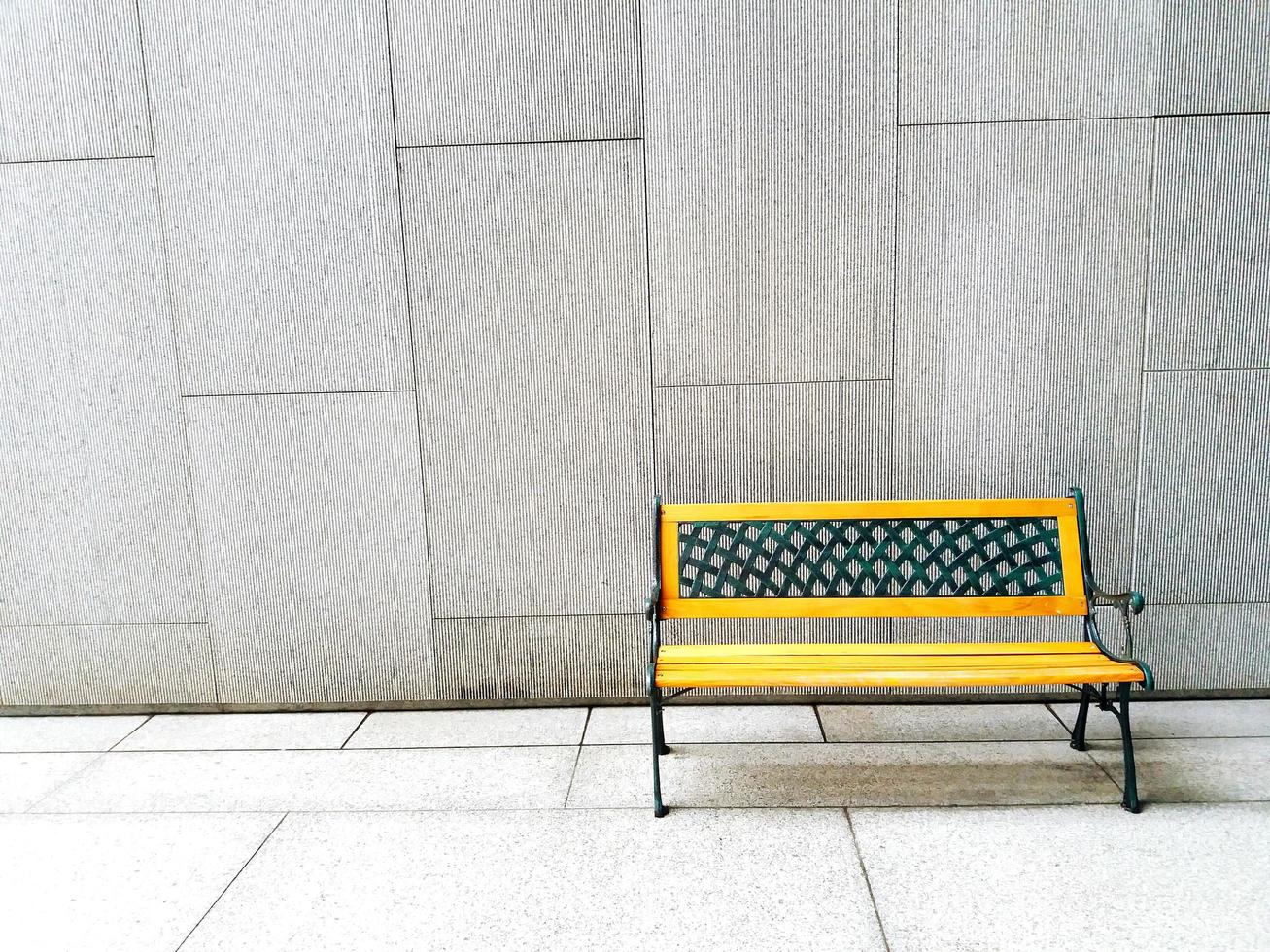Yellow bench on white or gray concrete wall background with copy space - available seat, alone and relaxing photo