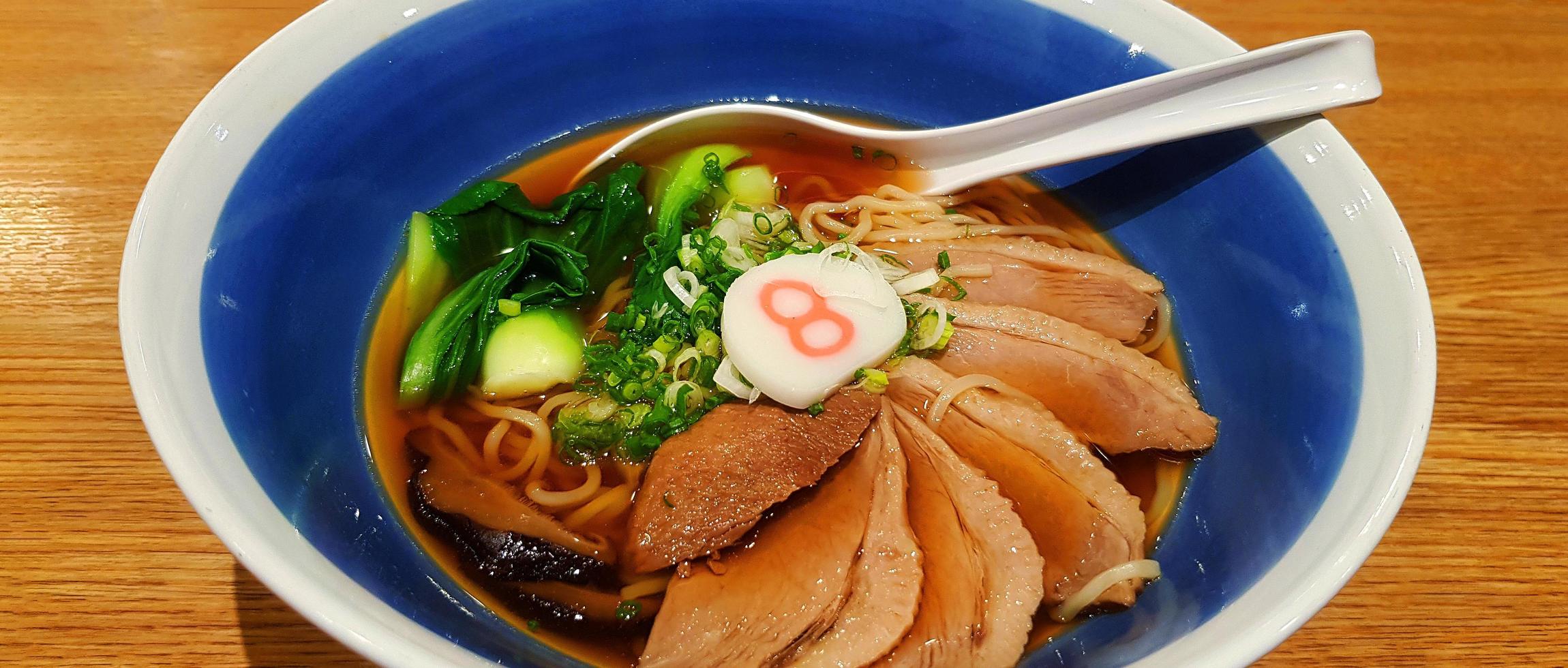 Hot ramen noodle with vegetable, sliced spring onion and pot-stewed duck in soup on blue bowl. Famous Japanese food on brown wooden background in Asia. photo