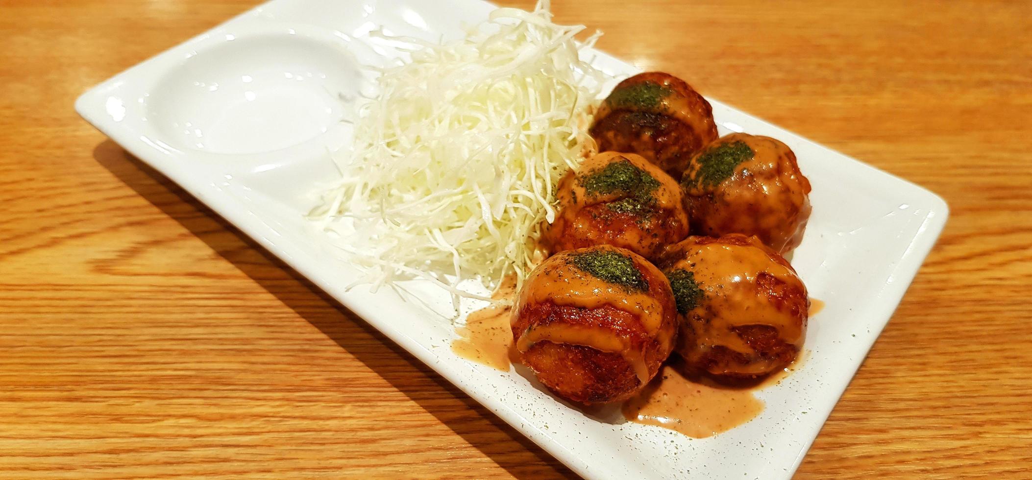 Takoyaki topped with sweet sauce and sliced cabbage in white dish on brown wooden background. Japanese food in plate on wood table with copy space. photo