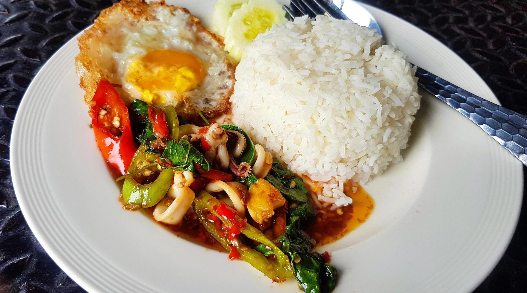 Close up Stir Fried Basil with squid and fried egg in Thai style on white plate or dish at  Thailand restaurant. Spicy food with rice. Famous meal in Asia. photo